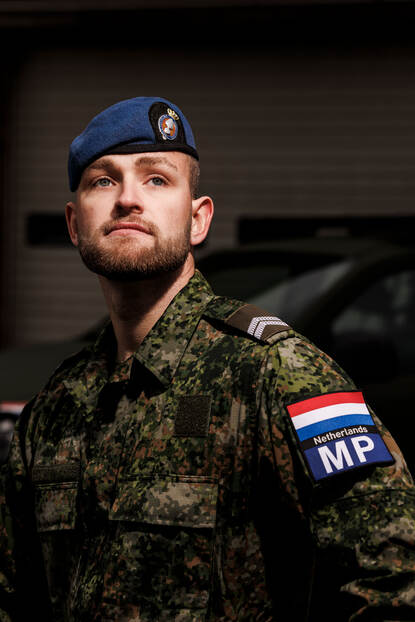 Portretfoto van marechaussee-1 Leense met blauwe baret op en armpatches van de Militaire Politie en een Nederlandse vlag.