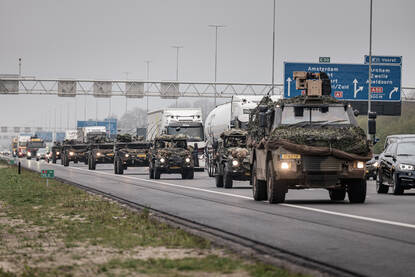 Militaire colonne rijdt op rechterrijstrook over snelweg. Het normale verkeer rijdt op de stroken daarnaast.