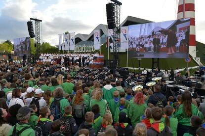 Een orkest treedt op op een goed gevuld plein, een muzikant bespeelt een blaasinstrument.