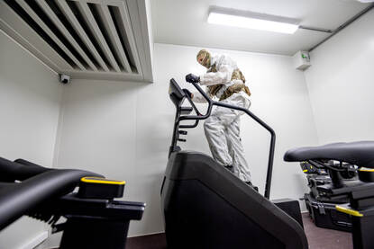 Een militair in wit pak loopt op een fitnessapparaat.