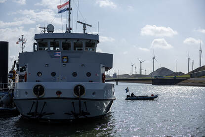 Boven het logo van Sandy Coast 2025 op de mouw van een marineman en duikondersteuningsvaartuig Zr.Ms. Nautilus aan de kade van Eemshaven. De DSS Galatea op zee en een rubber boot die over het water scheert.