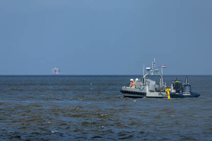 Boven: Op zee liggen een bootje van de marine en van de politie naast elkaar met de GeoSea op de achtergrond. Op de achterzijde van het bootje is de gele Seascan te zien. Daarna vaart de politie naast de Geosea. Onder: BNS Lobelia op zee en vervolgens gaat daarna een duikteami met een EOD’ers per rubber boot richting een mogelijk explosief.