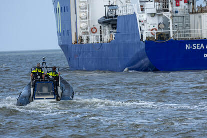 Boven: Op zee liggen een bootje van de marine en van de politie naast elkaar met de GeoSea op de achtergrond. Op de achterzijde van het bootje is de gele Seascan te zien. Daarna vaart de politie naast de Geosea. Onder: BNS Lobelia op zee en vervolgens gaat daarna een duikteami met een EOD’ers per rubber boot richting een mogelijk explosief.