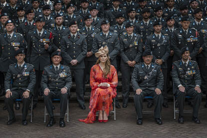 Een rood geklede prinses poseert te midden van militairen in deftig tenue.