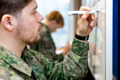 Een cadet schrijft iets op een whiteboard. Rechts close-up van een landkaart van het conflictgebied.