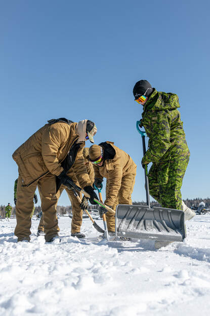 Een persoon in uniform steekt een grote, oranje sneeuwschep in de sneeuw.