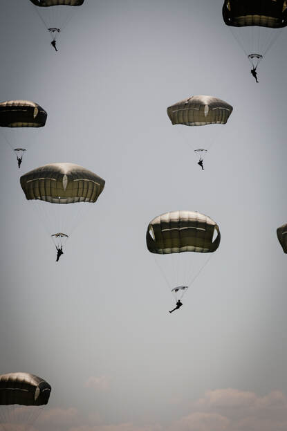 Parachutisten hangen naast elkaar in de lucht.