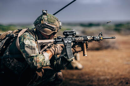Een geknielde marinier geeft een schot af, een huls springt door de lucht