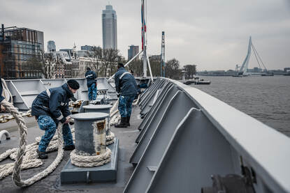 De nauten halen de trossen binnen, op de achtergrond de Erasmusbrug.