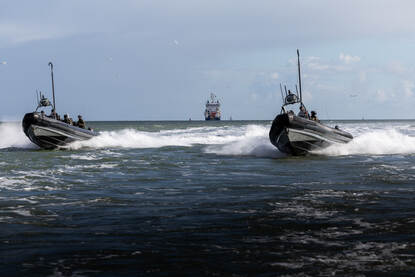 Op de linkerfoto houdt een operator een liggende verdachte onder schot. Op de rechterfoto varen snelle onderscheppingsboten richting de camera.