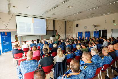 Groep militairen zit in een zaal en luistert naar een spreker.