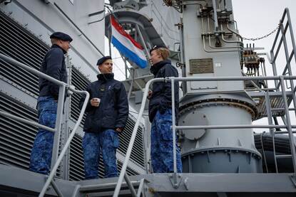3 jongens in marine-uniform drinken buiten op het schip een kop koffie.