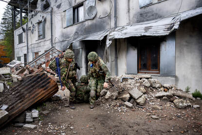 Twee militairen trekken een zogenaamd gewonde collega langs het gebouw door het puin.