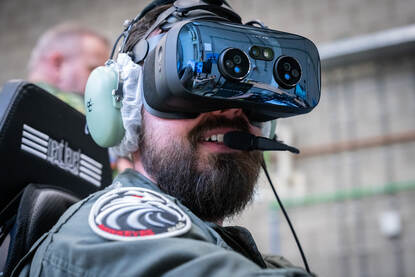 Een vlieger met een VR-bril op zij hoofd kijkt opzij. Daarnaast een foto van de stick die hij in zijn handen heeft.