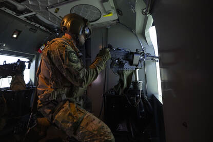 Vier afbeeldingen. Op een daarvan is een oplichtend bordje te zien met de tekst ‘trainer in use’. De andere drie foto’s tonen sergeant Michiel in de simulator en de virtuele wereld waarop hij uitkijkt vanuit de cabine van de Chinook. Ook is het boordwapen waarmee hij in de simulator werkt zichtbaar.