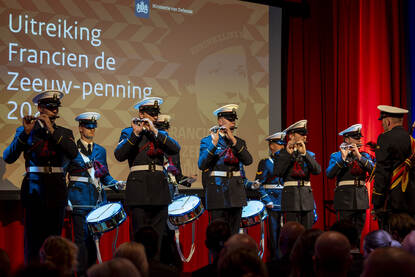 Muzikanten voor een scherm met daarop ‘Uitreiking Francien de Zeeuw-penning 2025’.