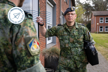 Luitenant-kolonel Léon van Hulst poseert met zijn tas onder zijn arm naast een gebouw.