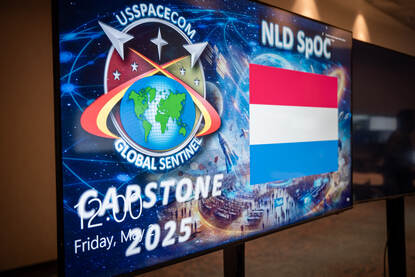 Afbeelding van een televisiescherm met daarop het logo van de oefening Global Sentinel en de Nederlandse vlag.