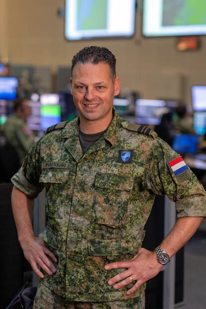 Militair met handen in de zij lacht in de camera.