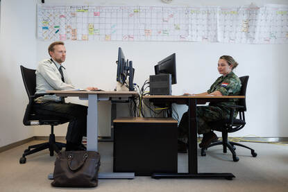 Karin achter haar bureau tegenover een landmacht militair aan zijn bureau.
