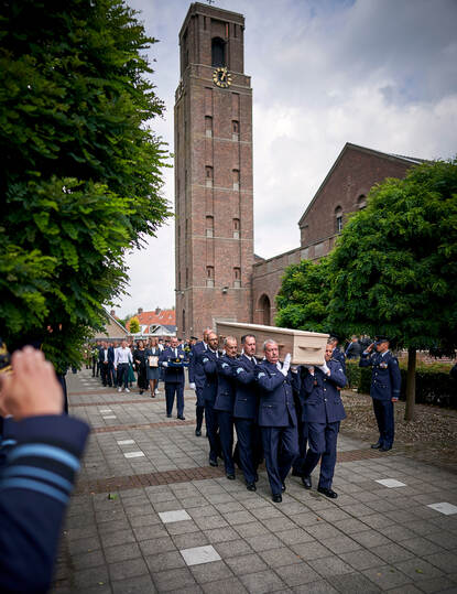 De draagploeg loopt met de kist op de schouders, daarachter een stoet mensen.
