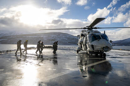 Afbeeldingen van een Chinook, een NH90, een MQ-9 Reaper en twee F-35’s die over een marineschip vliegen.