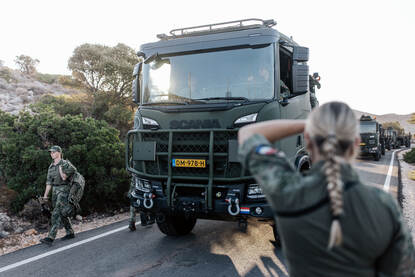 En vrouwelijke militair ziet toe op het veilig manoeuvreren van een colonne militaire vrachtwagens.