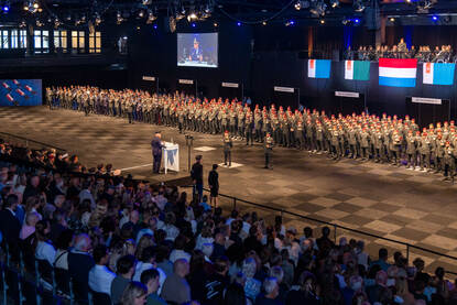 Volle zaal met rijen opgestelde militairen.