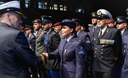 Vrouwelijke luchtmachtmilitair, die staat opgesteld tussen militairen van de andere drie krijgsmachtdelen, wordt de hand geschud tijdens de medaille-uitreiking.