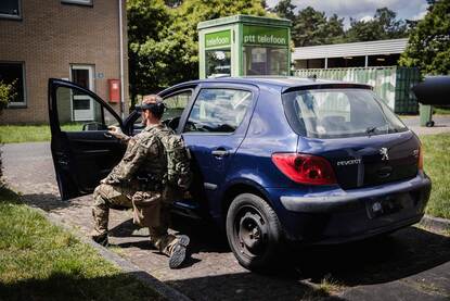 Militair met VR-bril onderzoekt een auto.