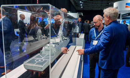 Twee mannen in blauw pak bij een maquette van een Anti Submarine Warfare-fregat in een vitrine.