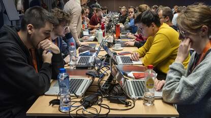 Lange tafel met aan twee kanten mensen met laptops.