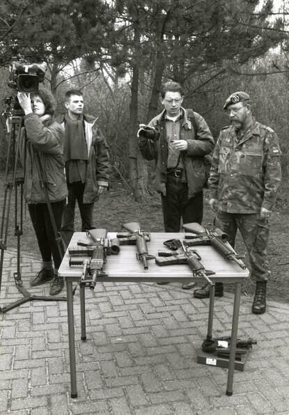 Tafel met vier Diemaco-varianten met daarachter journalisten en een adjudant in camouflage-uniform.