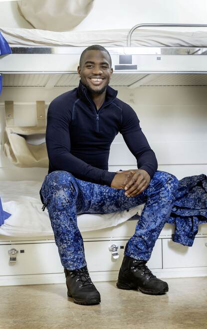 Een militair van de vloot zit  in de nieuwe blauwe gevechtskleding op een bedje aan boord van een marineschip.