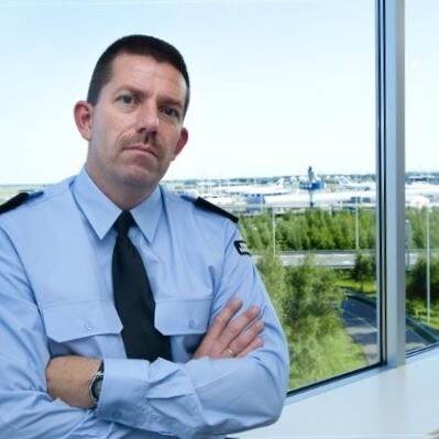 Een lid van de KMar zit in tenue en met armen over elkaar in vensterbank.