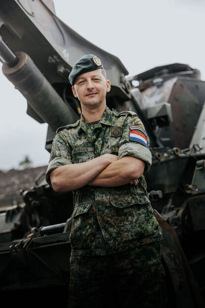 Majoor JIlles kijkt in de camera. Hij draagt een groene baret en een vlekkenpak. Achter hem is vaag de Kodiak te zien.