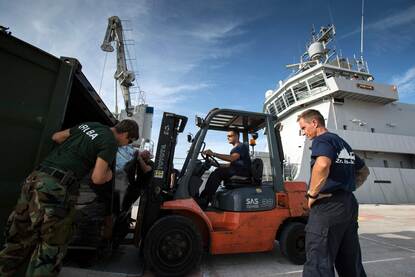 Twee foto’s van de Pelikaan tijdens het lossen van hulpgoederen in een haven.