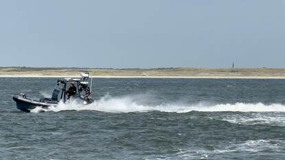Een rubberboot met 2 mensen aan boord laat flinke golven achter op zee.