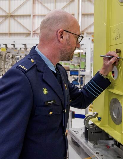 Een man in uniform schrijft iets op een groot geel metalen vlak.